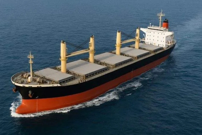 A large dry bulk carrier sailing across the ocean, viewed from above.