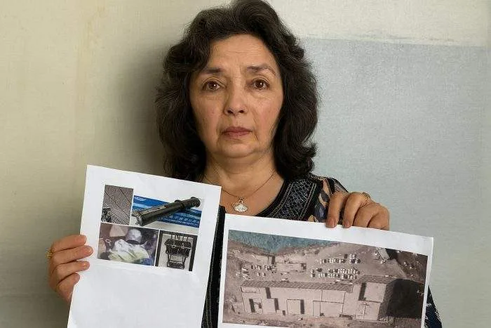 a woman holding documents with photos and satellite images as evidence of Xinjiang camps, looking directly into the camera with a serious expression.