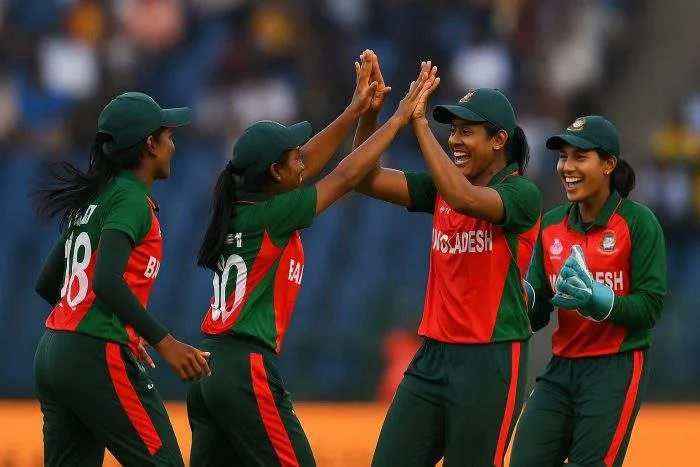 Four Bangladeshi women cricketers celebrate a wicket during the Women’s Cricket World Cup in Guwahati, wearing red-and-green team jerseys under bright sunlight.