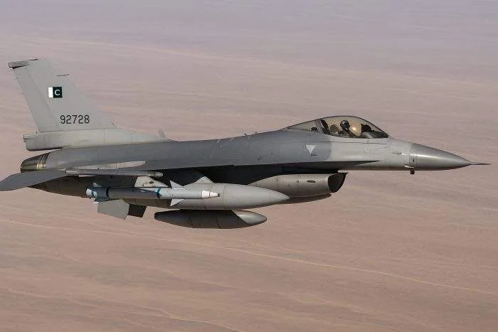 Pakistan Air Force F-16 fighter jet flying over arid terrain, equipped with AIM-120 missiles under its wings.