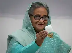 A close-up of a television screen showing a blurred broadcast of Sheikh Hasina, with a silhouette of a person watching in the foreground, representing the virtual meetings held from Kolkata.