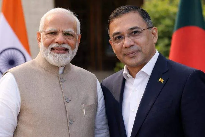 Indian Prime Minister Narendra Modi and Bangladesh Prime Minister Tarique Rahman standing side by side during a diplomatic moment, with blurred national flags in the background.