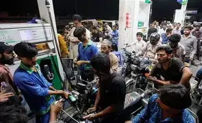 A wide-angle shot of a PSO petrol station in Karachi at night, with a line of hundreds of motorcycles and cars stretching down the block, and a "No Petrol" sign hung on a stationary pump.