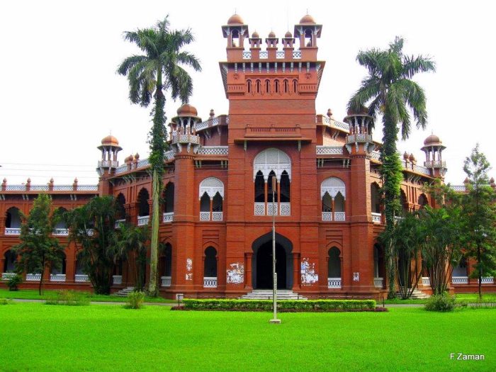 Front view of Curzon Hall at Dhaka University, a historic red-brick academic building with arches, towers, and palm trees in the foreground.