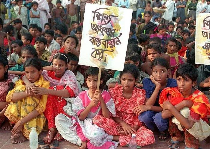 The central administrative building of a prominent human rights body in Dhaka, with placards condemning child abuse visible near the entrance.