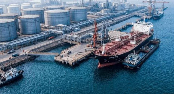 A professional graphic showing a large oil tanker at a terminal with holographic overlays of the U.S. Treasury seal and a map of the South China Sea.