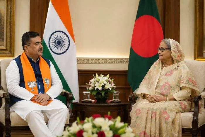 Former Bangladesh Prime Minister Sheikh Hasina and West Bengal Chief Minister Suvendu Adhikari sit across from each other during a formal diplomatic-style meeting, with the flags of Bangladesh and India displayed in the background.
