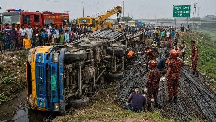 Rescue workers and local residents gather around an overturned truck carrying iron rods after a deadly highway crash near the Jamuna Bridge in Tangail.