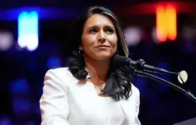 Outgoing DNI Tulsi Gabbard walking away from a press briefing room inside the White House, with officials watching from the sidelines.