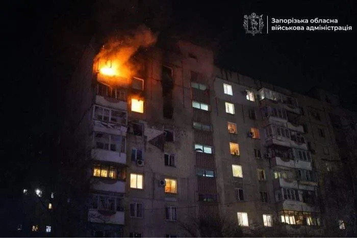 Firefighters battling a massive blaze engulfing a struck high-rise residential building in Kyiv under a dark night sky.