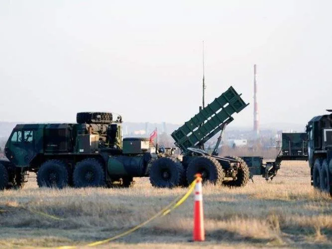 A truck-mounted Patriot missile launcher angled skyward, firing a bright rocket booster trail into the early dawn clouds.