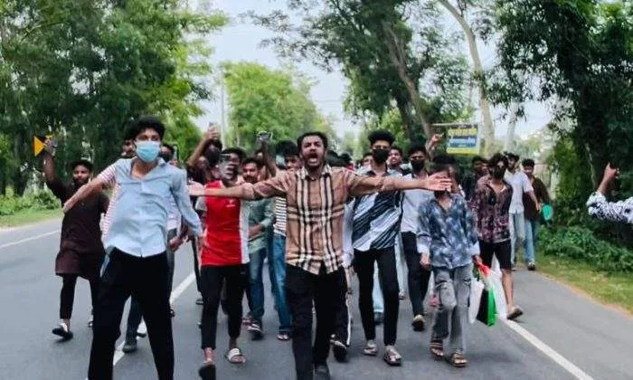: A large crowd of student demonstrators blocking a wide highway, standing around a pile of burning tires emitting black smoke.