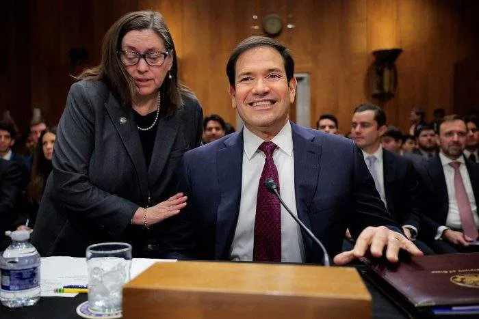 Secretary of State Marco Rubio gesturing emphatically while testifying before a packed, microphoned Senate congressional committee room.