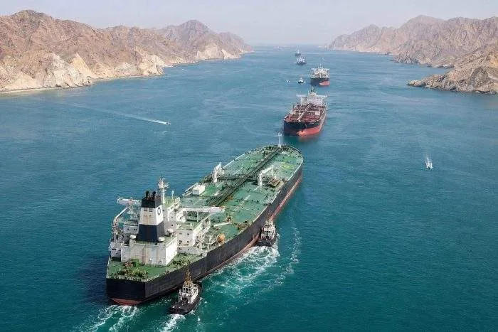 Horizontal wide shot of commercial shipping vessels and oil tankers navigating through the southern channel of the Hormuz Strait.