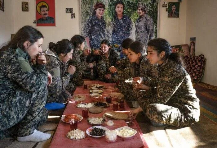 A wide-angle, high-definition photograph of a group of female soldiers wearing full military combat gear and backpacks, training intensely during an outdoor endurance drill under daylight.