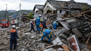 Horizontal shot showing emergency rescue workers searching through collapsed building debris in Kumamoto Japan.